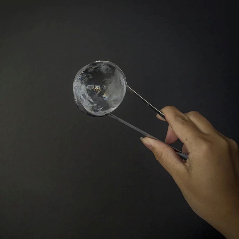 Crystal-clear ice sphere 5.5cm held in tongs, Malaysia